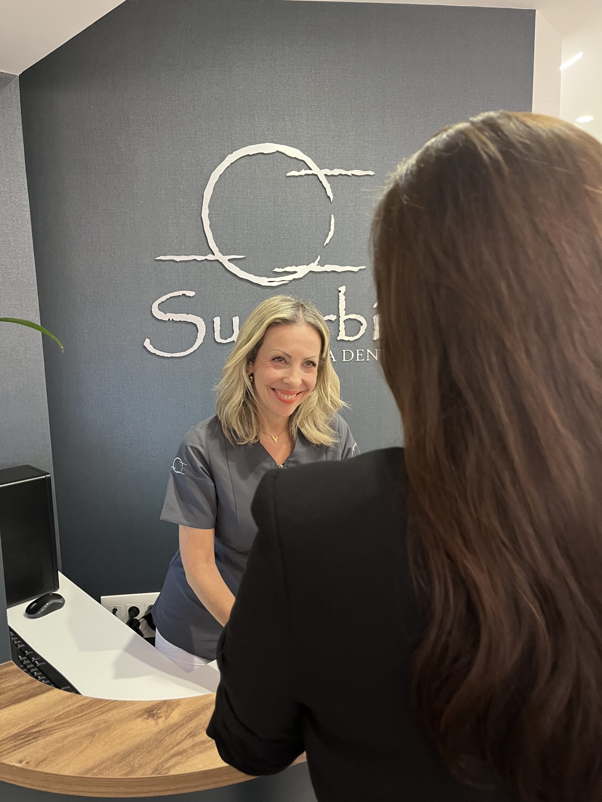 Recepcionista de Clínica Dental Superbia en el mostrador de bienvenida, entorno moderno y profesional.